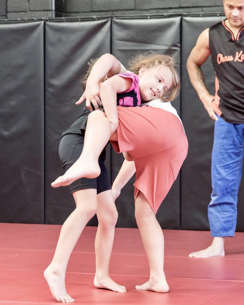 Two children practising a takedown in a kids martial arts class at Chau Kaizen while a coach watches