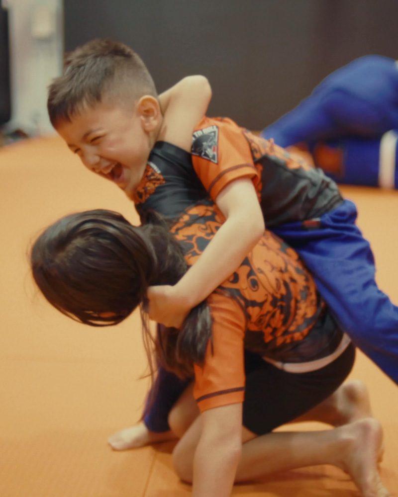 Two children laughing while grappling in a kids MMA class at Chau Kaizen in Prospect