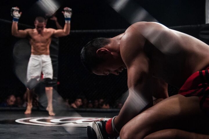 Suasday Chau on his knees in the cage after an MMA fight, his opponent standing behind him with arms raised